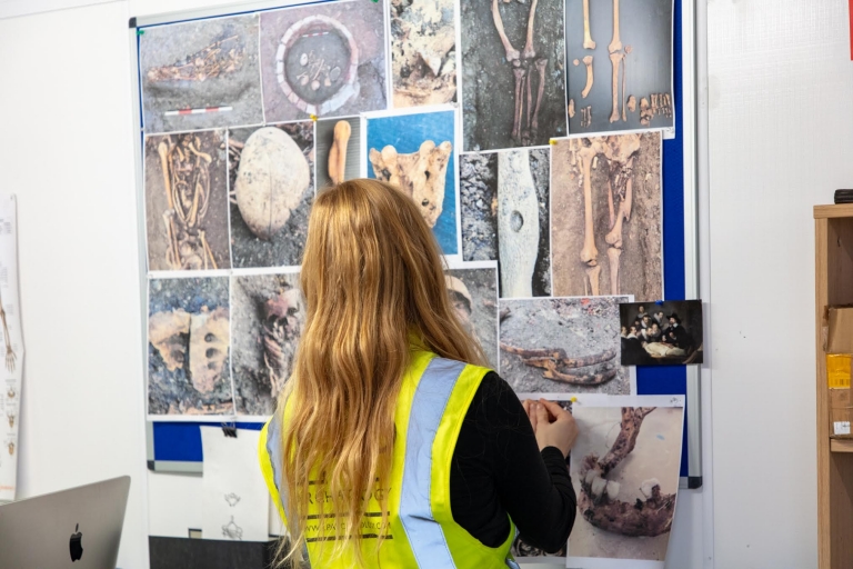 A long haired person looks at a wall full of photos of human bones.