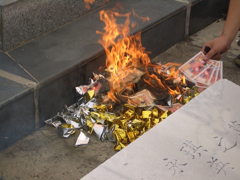 Paper money is on fire in a pile mixed with shiny gold paper.