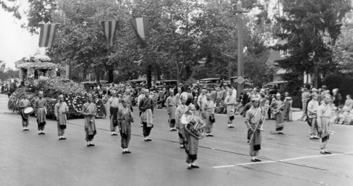 A black and white photo showing a group of Chinese boys performing as a marching band down the street.