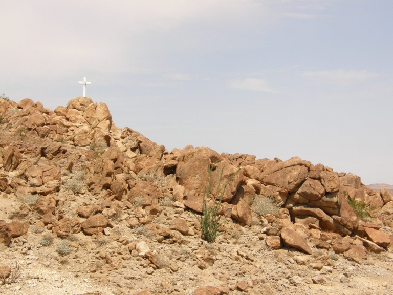 A massive pile of rocks with a white cross on top of it.