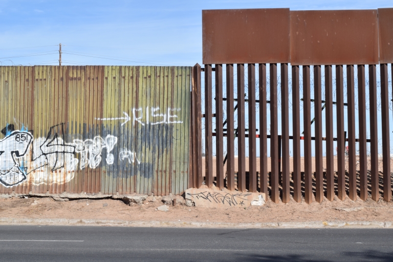 A rusted iron fence next to a fence covered in graffiti.