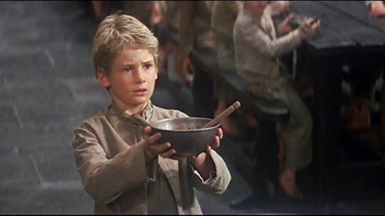 A scene from the movie Oliver Twist where Oliver holds out a bowl of soup