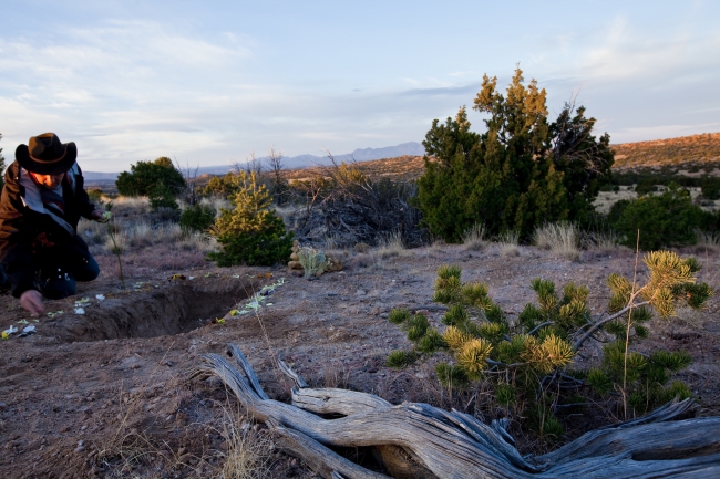 Photo of a man wearing a cowboy hat placing flower petals around the edge of a natural burial plot.