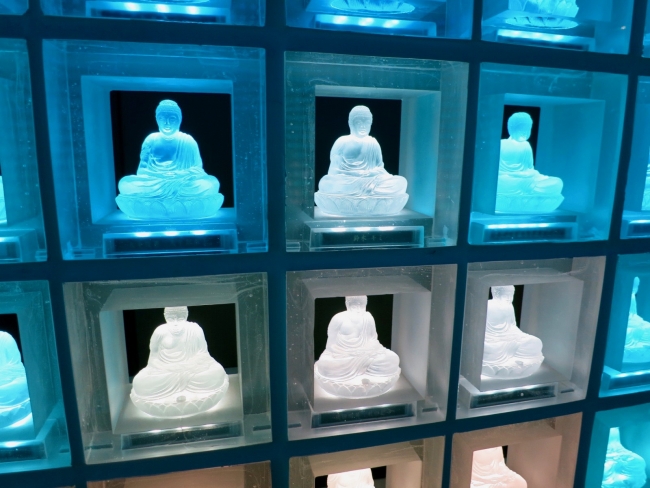 Photo of a section of a Japanese columbarium, where LED buddha glass statues sit on a gridded shelf in place of tombstones.