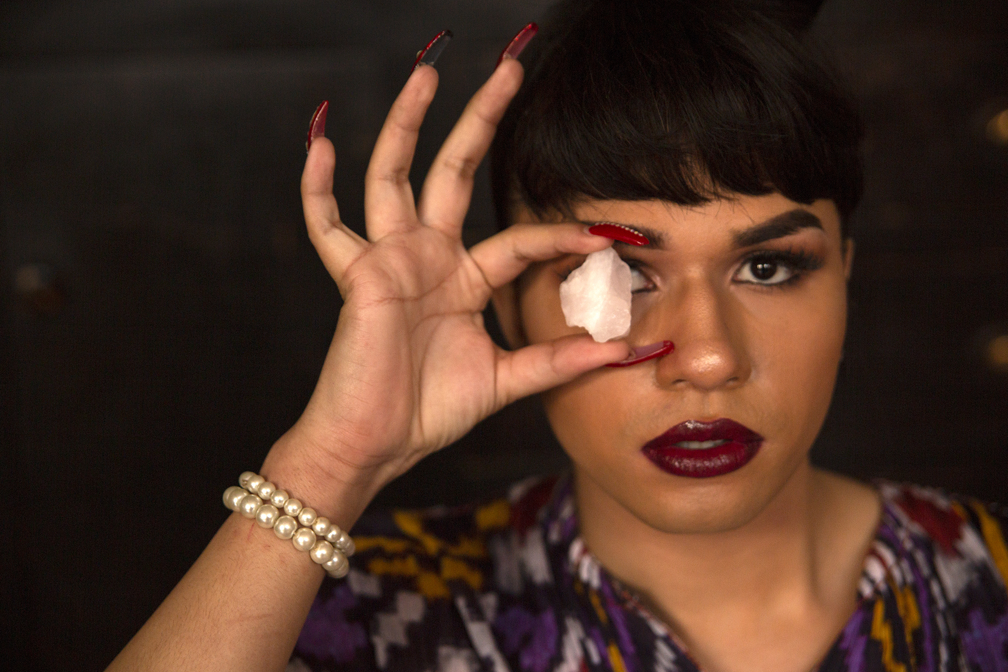 a person holds a small crystal up over one of their eyes