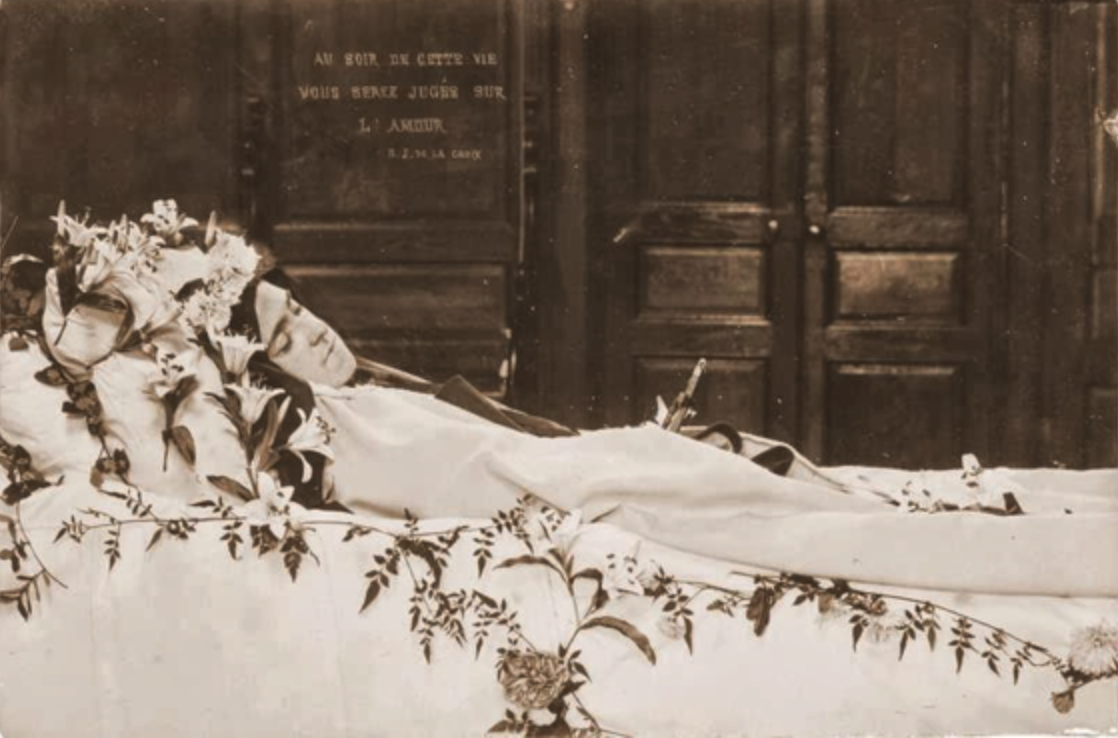 St Therese of Lisieux's body wearing a nun's habit while lying on a white bed surounded by flowers