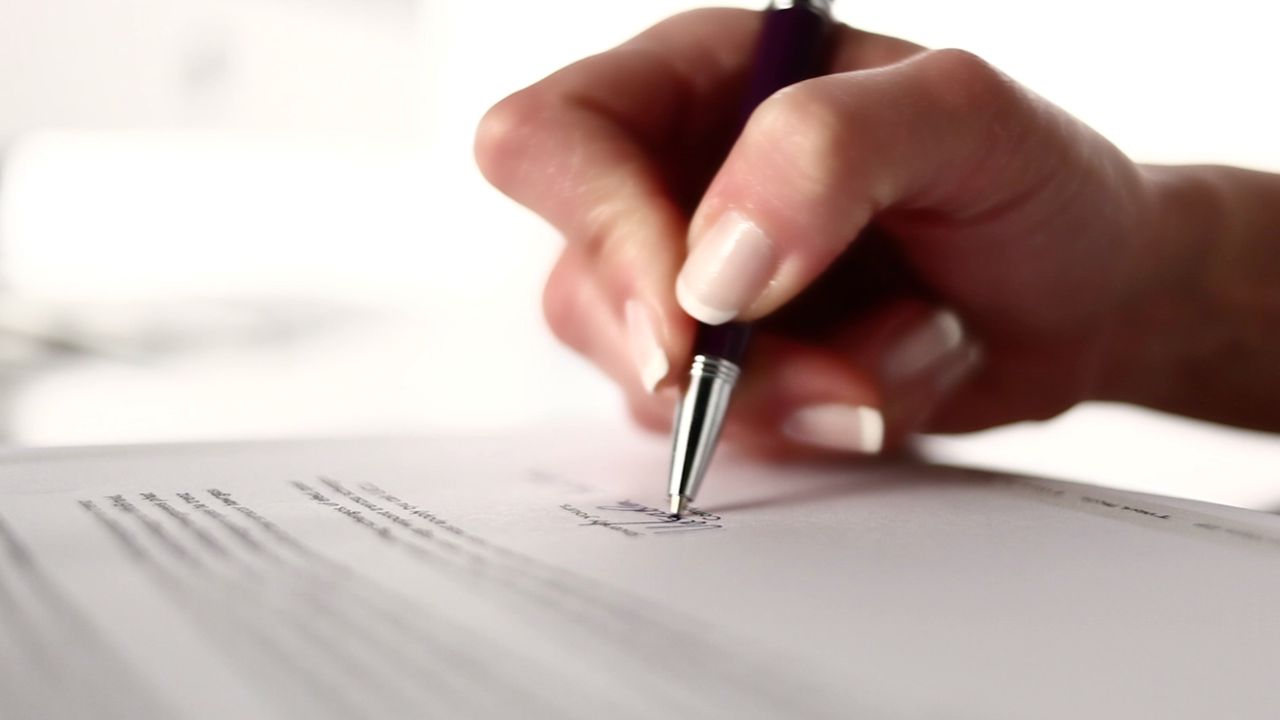 a dark skinned hand holds a pen and writes on a white sheet of paper