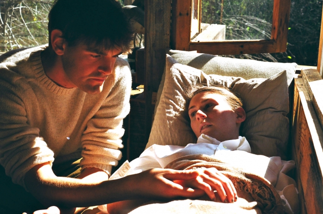 Photo of a man holding the hand of a deceased woman at a home funeral