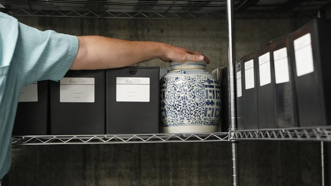 Aan arm with light skin touches the top of an urn on a shelf