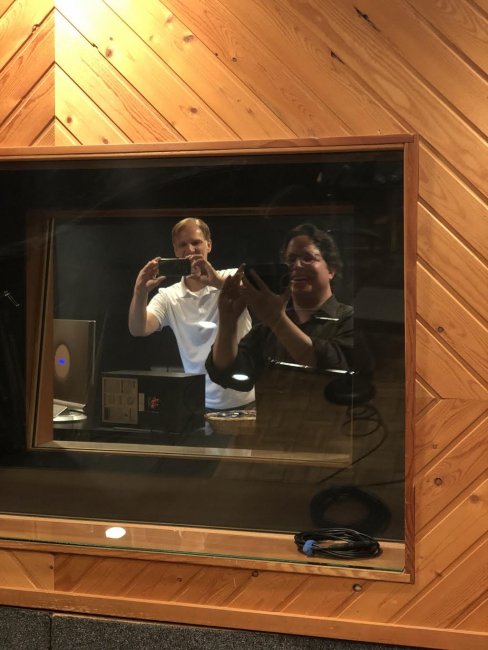 Paul Tavener and Dory Bavarsky taking photos on their cell phones through the recording studio window.