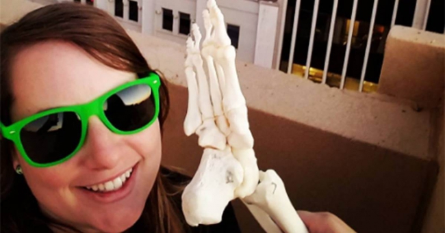 Photo of a woman wearing lime green sunglasses holding a foot skeleton like a phone.