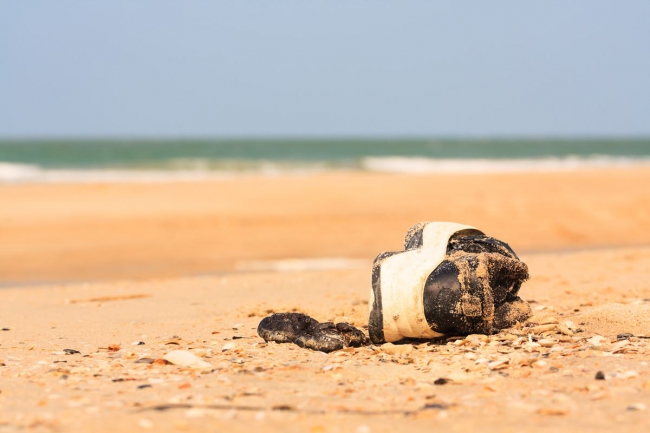 Photo of a lone sneaker covered in sand sideways on a beach.