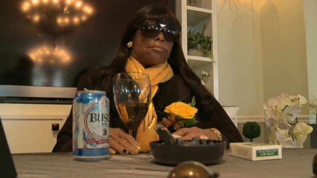 Photo of Miriam Burbank sitting at a table with a wineglass, flowers, and ash tray.