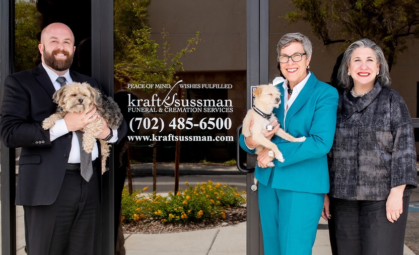 A man and two women holding small dogs stand outside the door of a funeral home