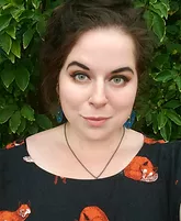 Headshot of light skinned woman with dark hair pulled back, wearing a black shirt with red accents