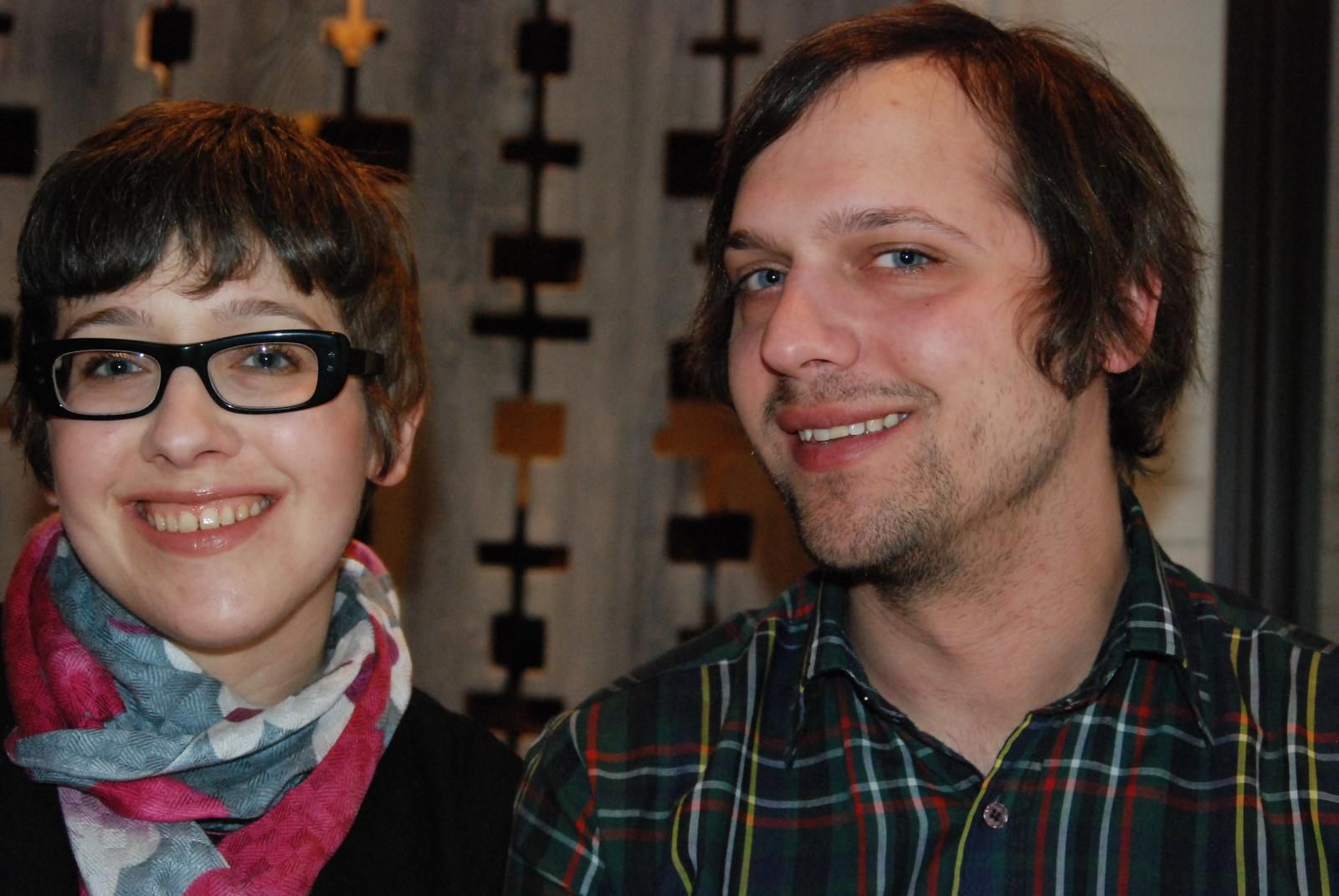 Close up of Nikki, wearing glasses, and Chris standing close to each other and smiling at the camera.