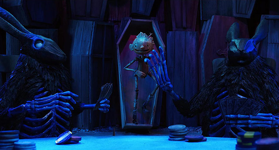 Pinnocchio emerges from a standing coffin, interrupting a couple skeletal rabbits seated at a table playing cards.