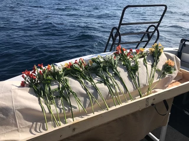 A shrouded body covered in flowers near the ocean