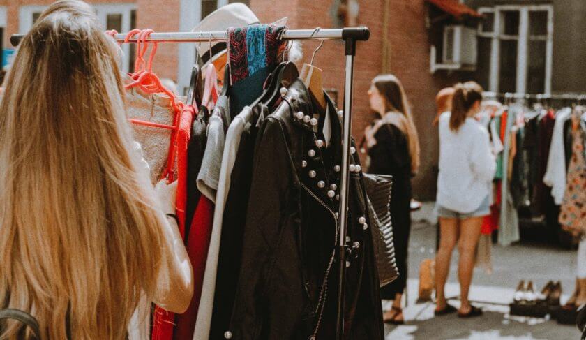 Racks of clothing are displayed outside as people shop