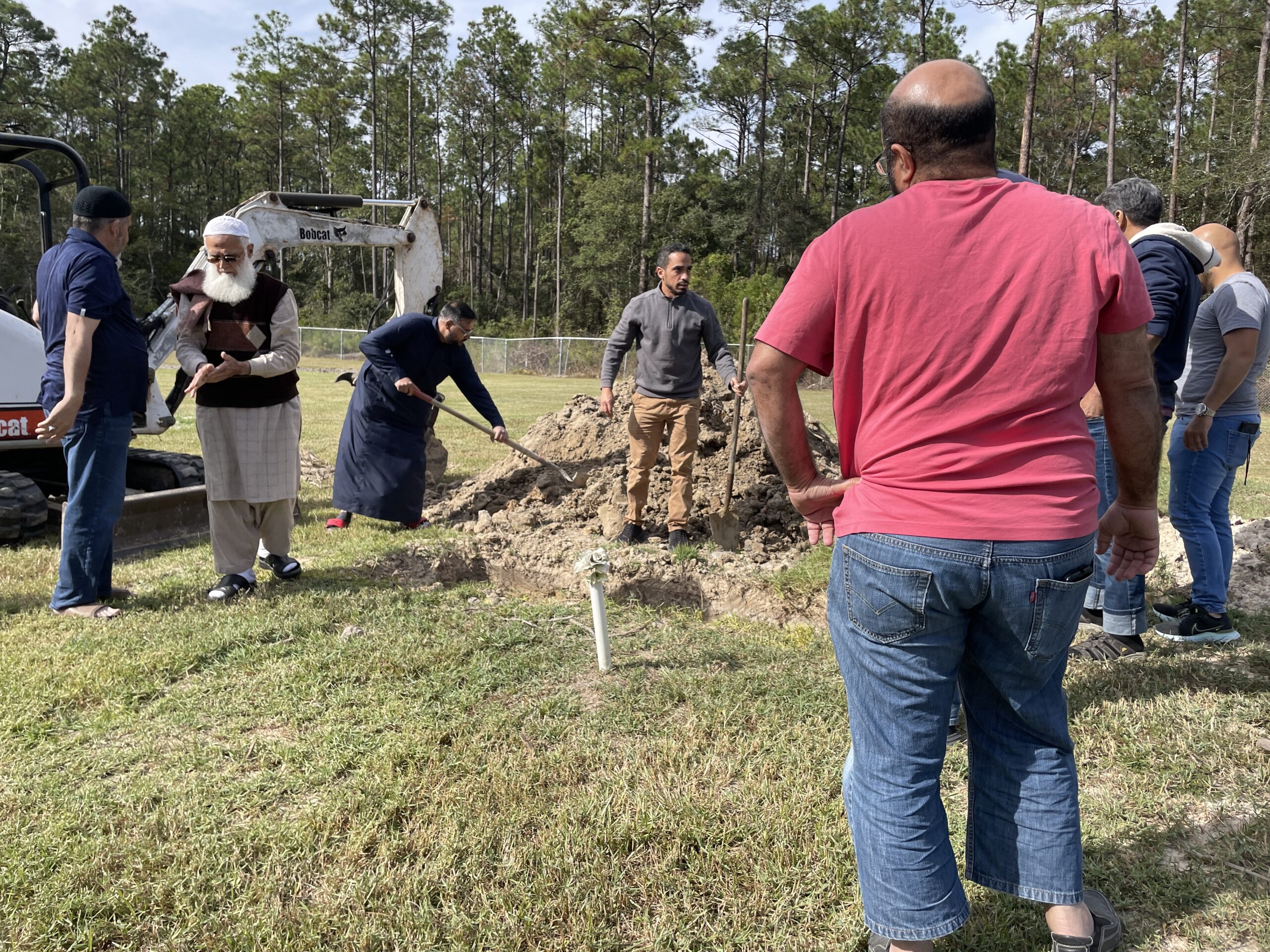 Photograph at a cemetery, people are facilitating a traditional Muslim burial