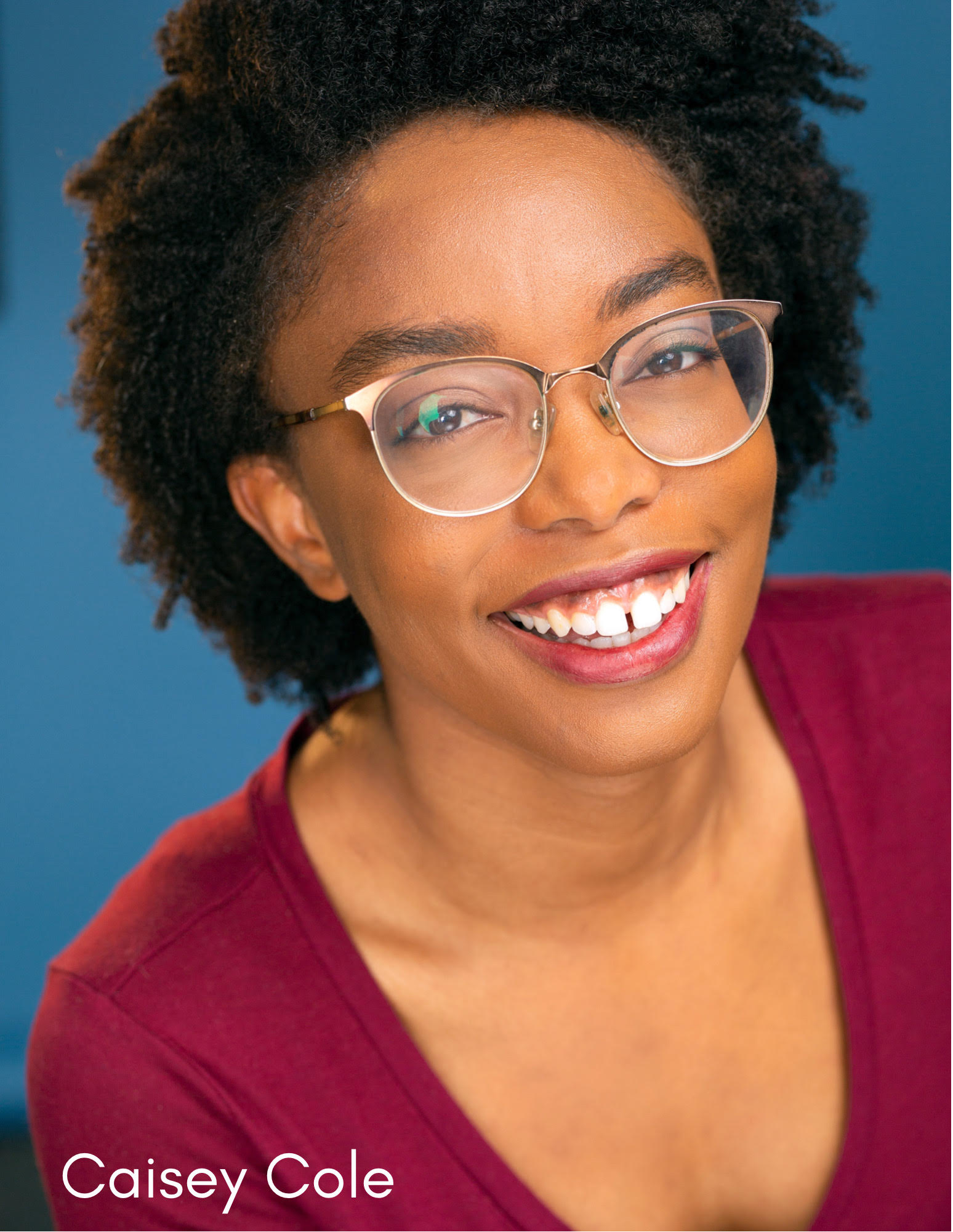 Headshot of actress Casey Cole, a woman wearing glasses and a deep red colored shirt, smiling at camera