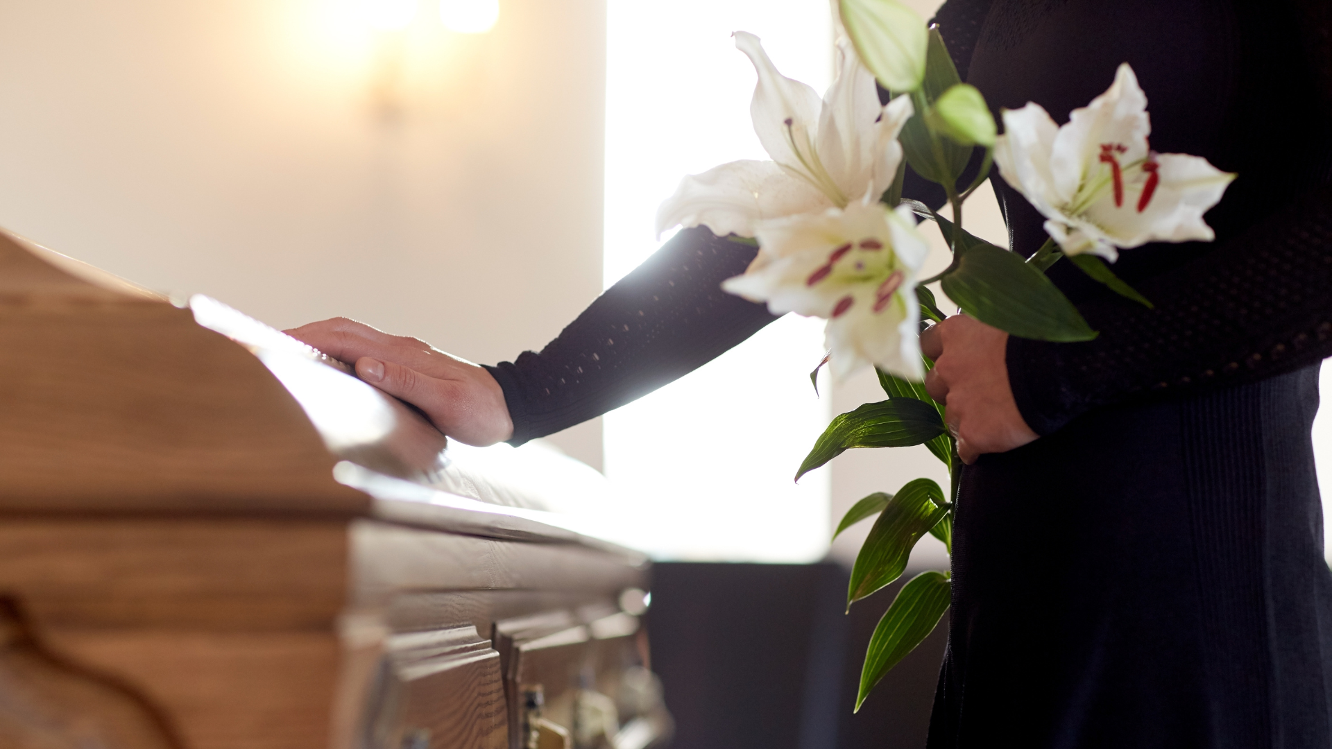 photo of a person dressed in black. In one hand they are holding flowers and in the other reaching out to touch coffin