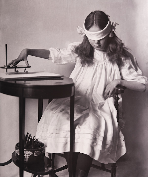 black and white vintage photo of a a young girl operating a planchette