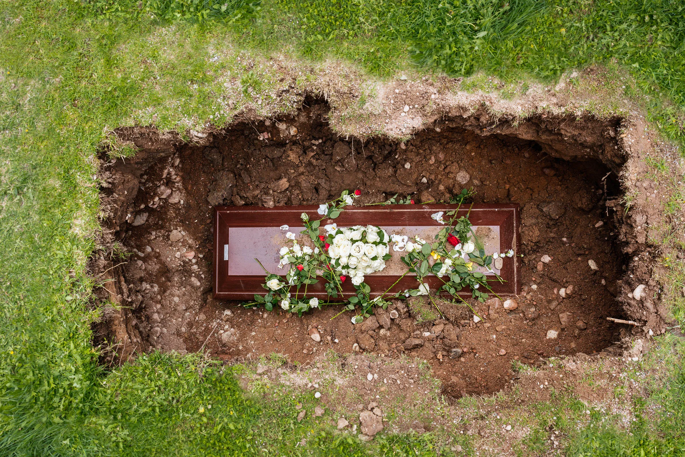 photo of an open grave with a coffin inside, covered with flowers