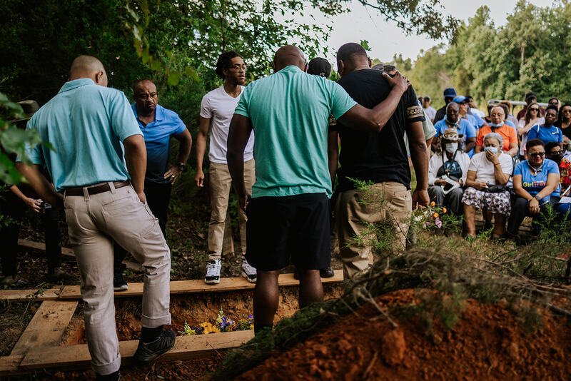 A photo of African American men standing around an open grave in a conservation burial ground.