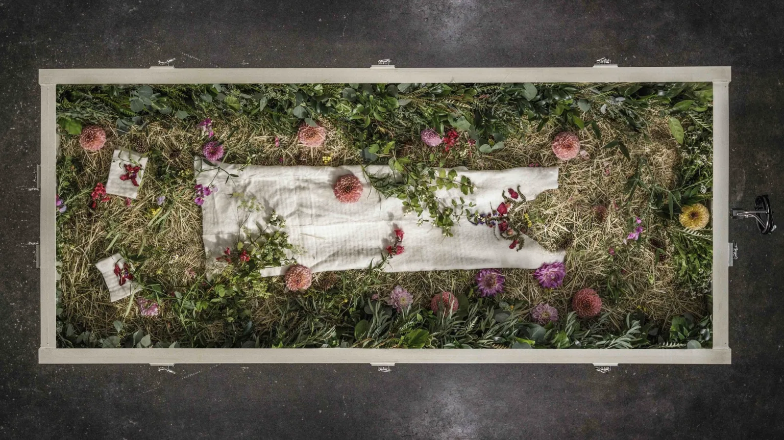Image of a body in a white shroud laid out in a vessel at Return Home. The body is covered in natural material and flowers